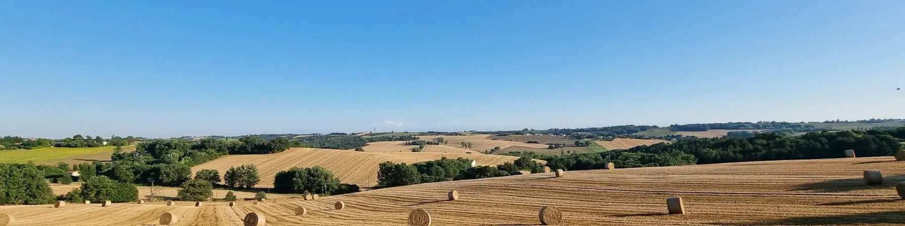 Paysage des coteaux de Rebigue : champs moissonnés et balles de foin sous un ciel bleu
